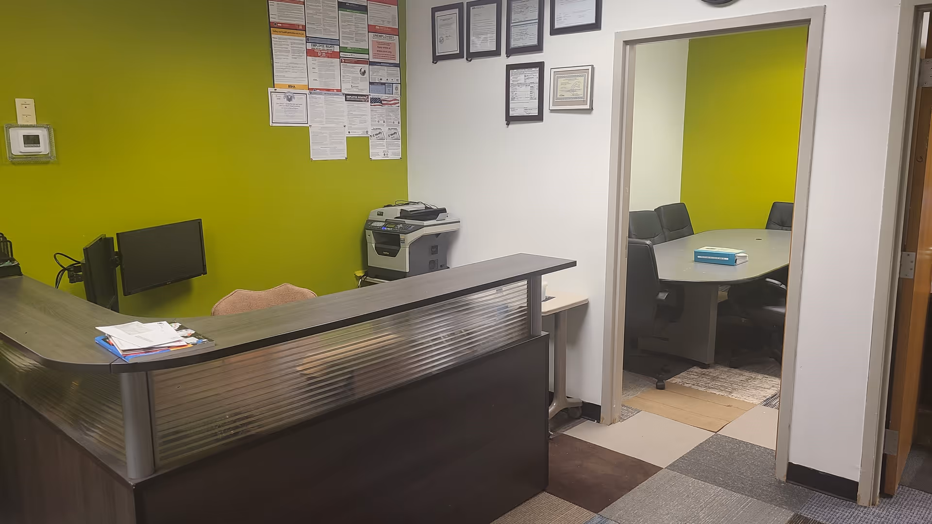 Reception desk in a lime-green interior with a meeting room visible through a doorway.