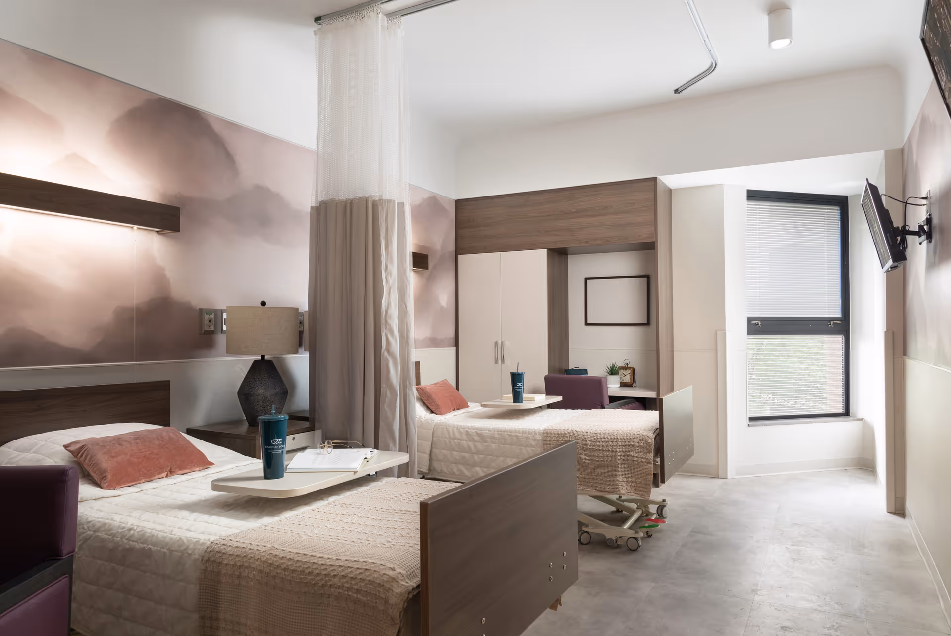 Two hospital beds in a modern patient room with a privacy curtain and window.