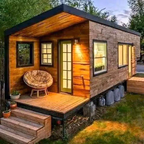 Small wood-clad building with a lit front door, porch, and circular chair.