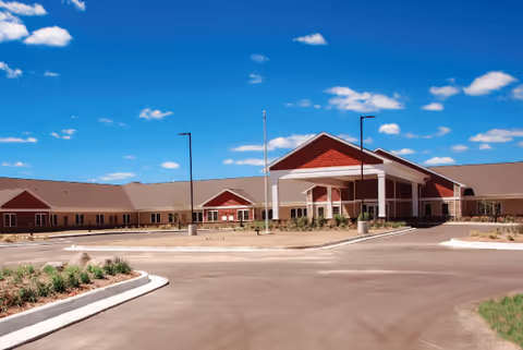 A single-story senior living facility with red accents and a covered entrance on a paved lot.