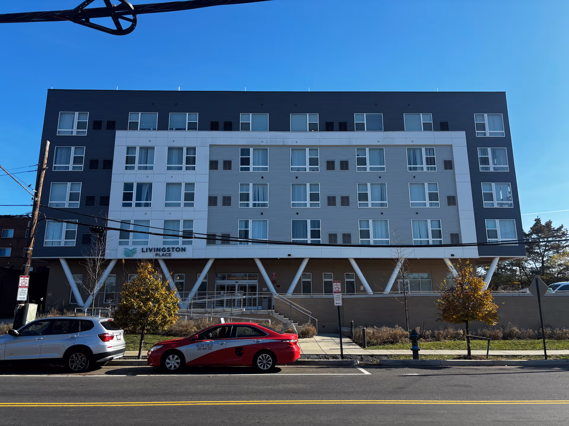 Facade of a modern multi-story building labeled "Livingston Place" with parked cars and a sidewalk in front.