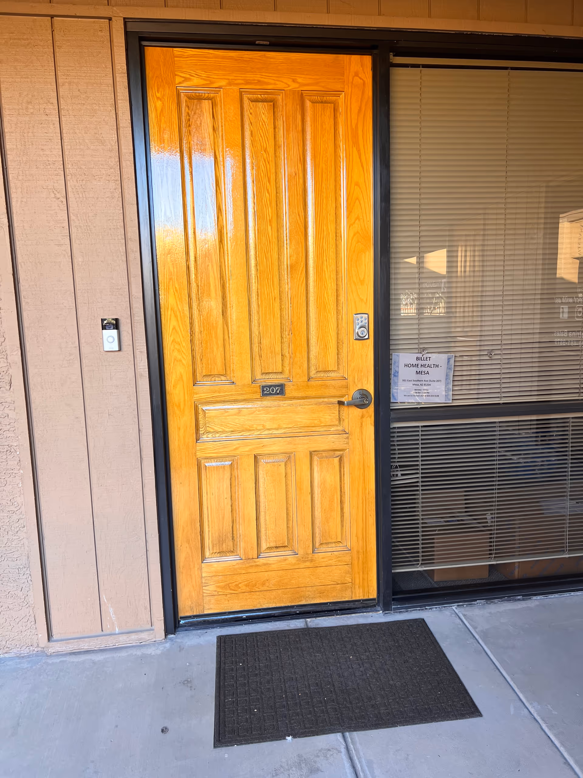 Wooden front door of Billet Home Health Mesa with blinds and a welcome mat.