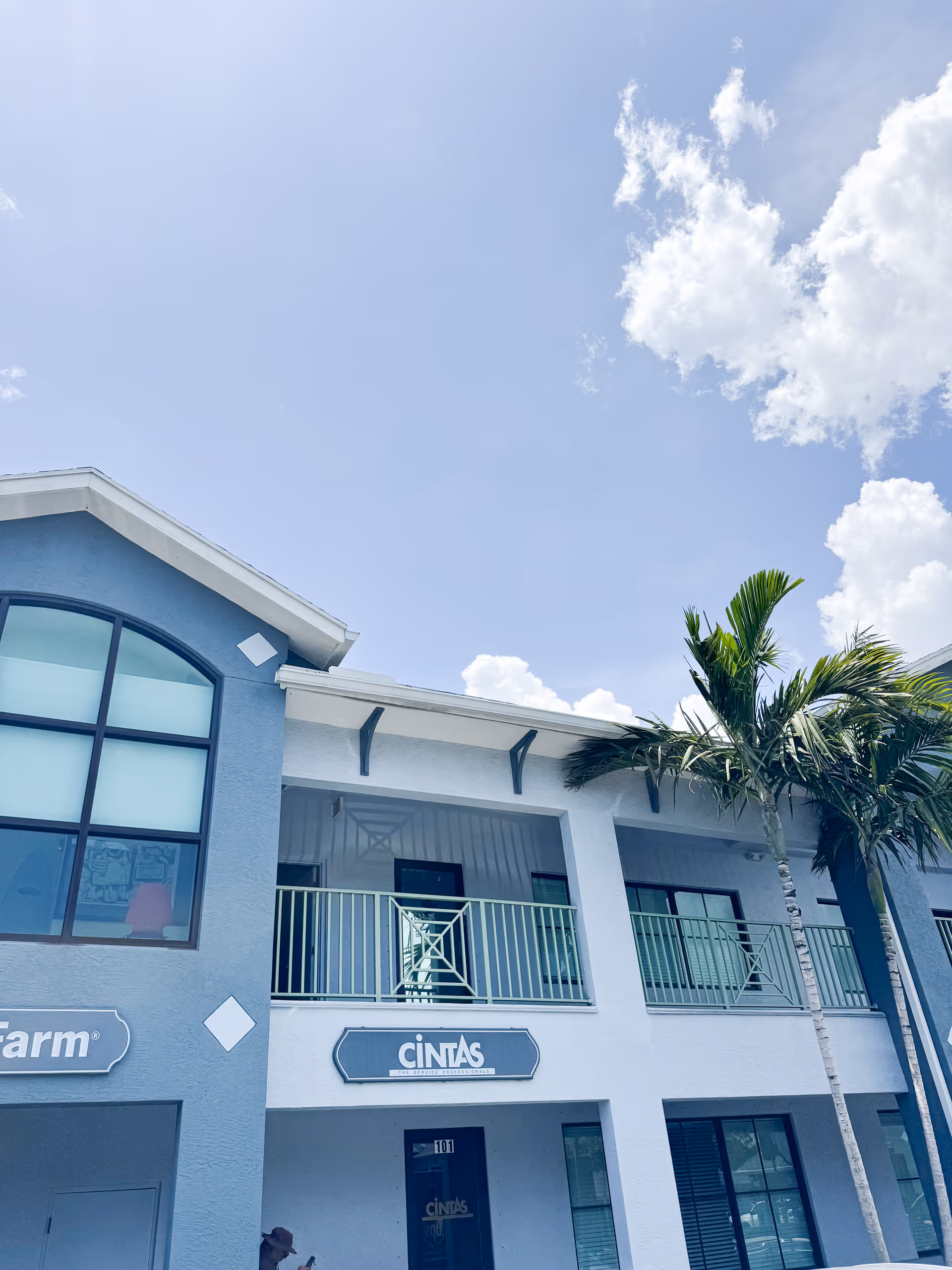 Blue two-story senior living facility with balconies, palm trees, and a clear blue sky.