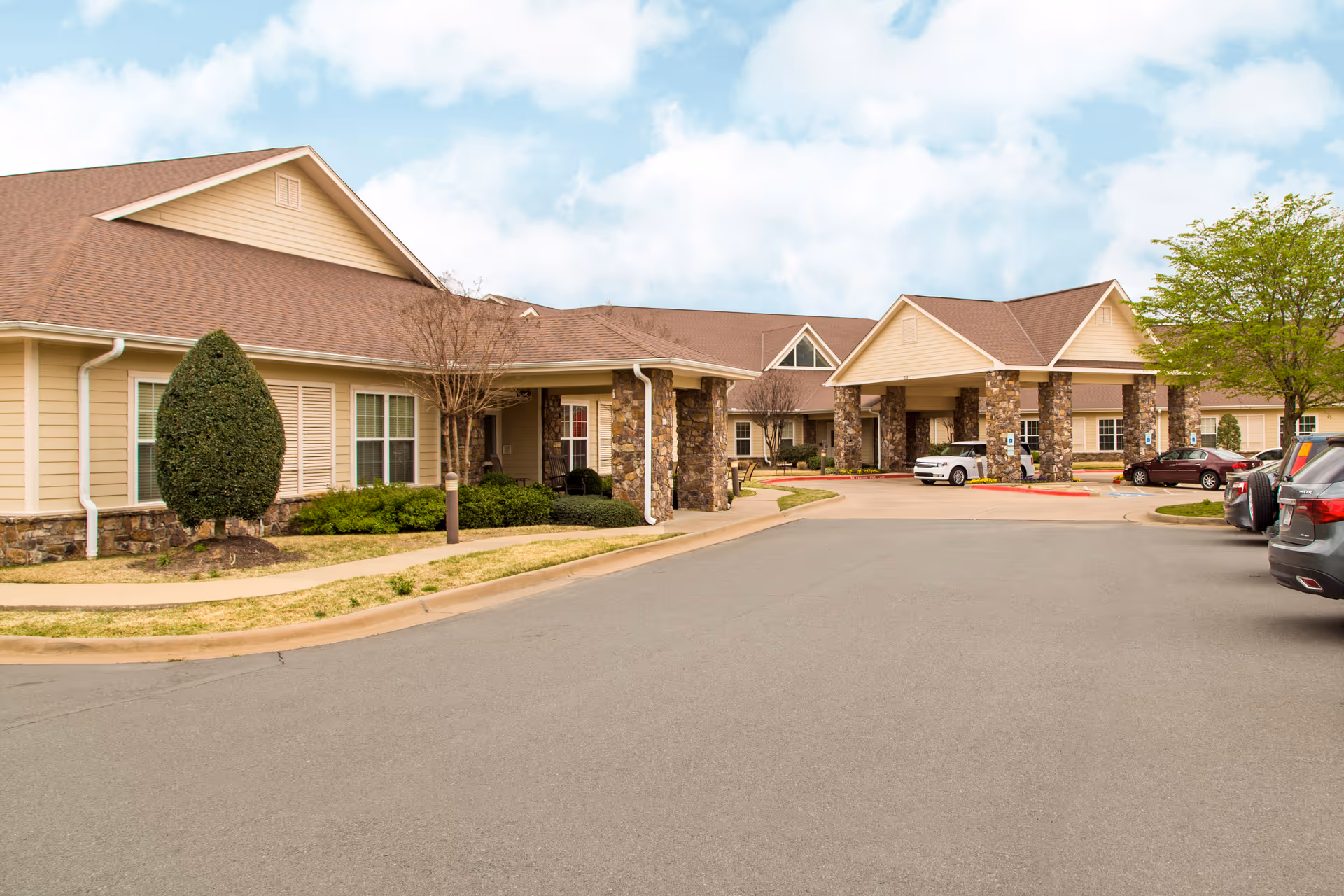 Exterior view of Brookdale Chenal Heights facility with a covered entrance and parked cars.