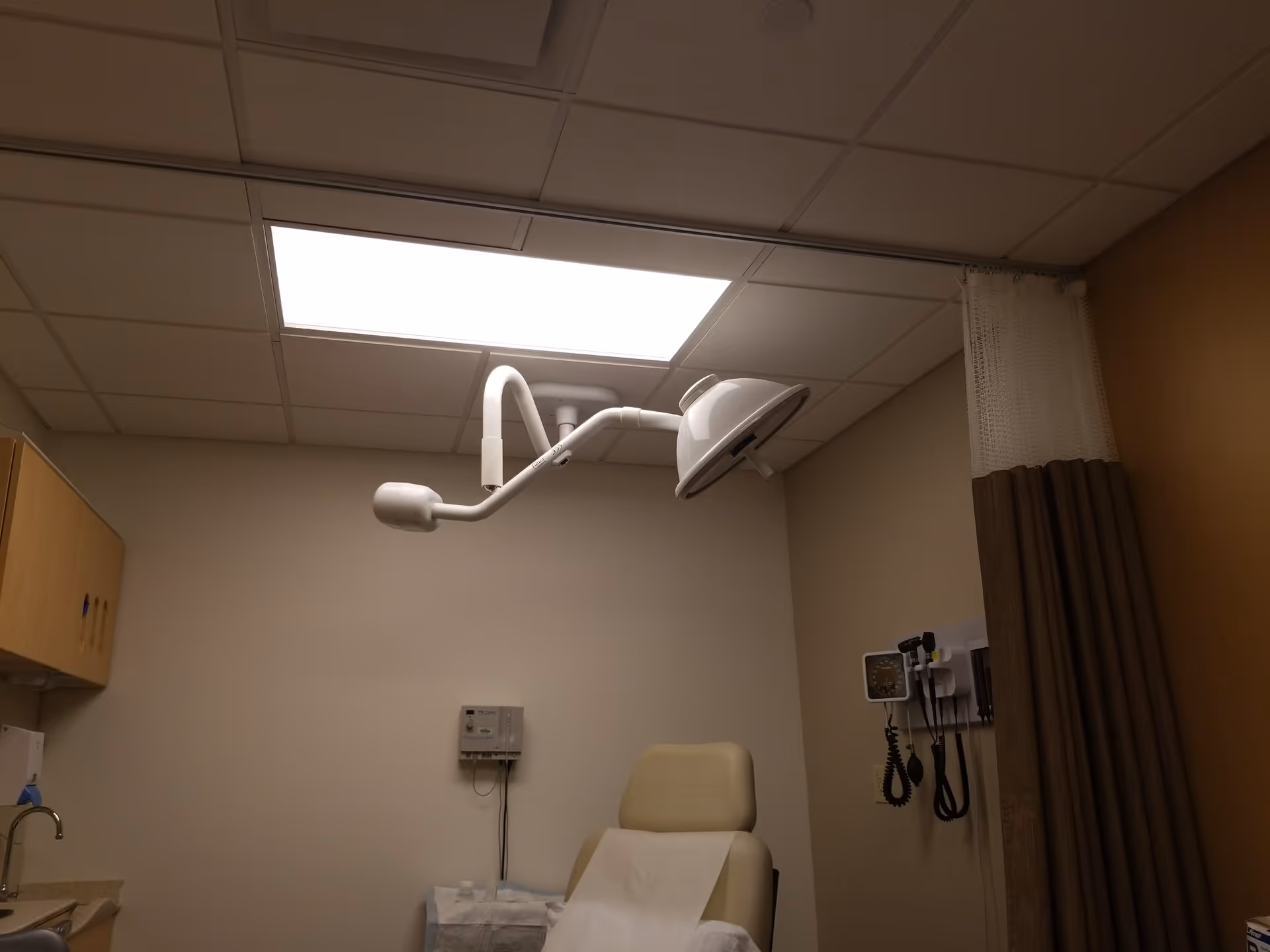 Interior medical examination room with an adjustable chair, overhead light, and equipment.