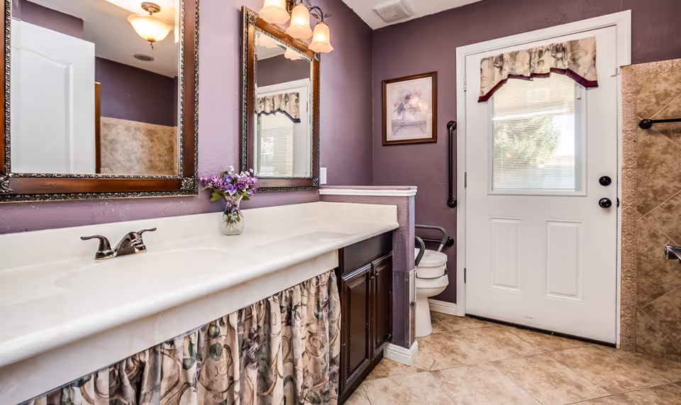 Bathroom with a long vanity and sink, two mirrors, a toilet, and an exterior door against purple walls.