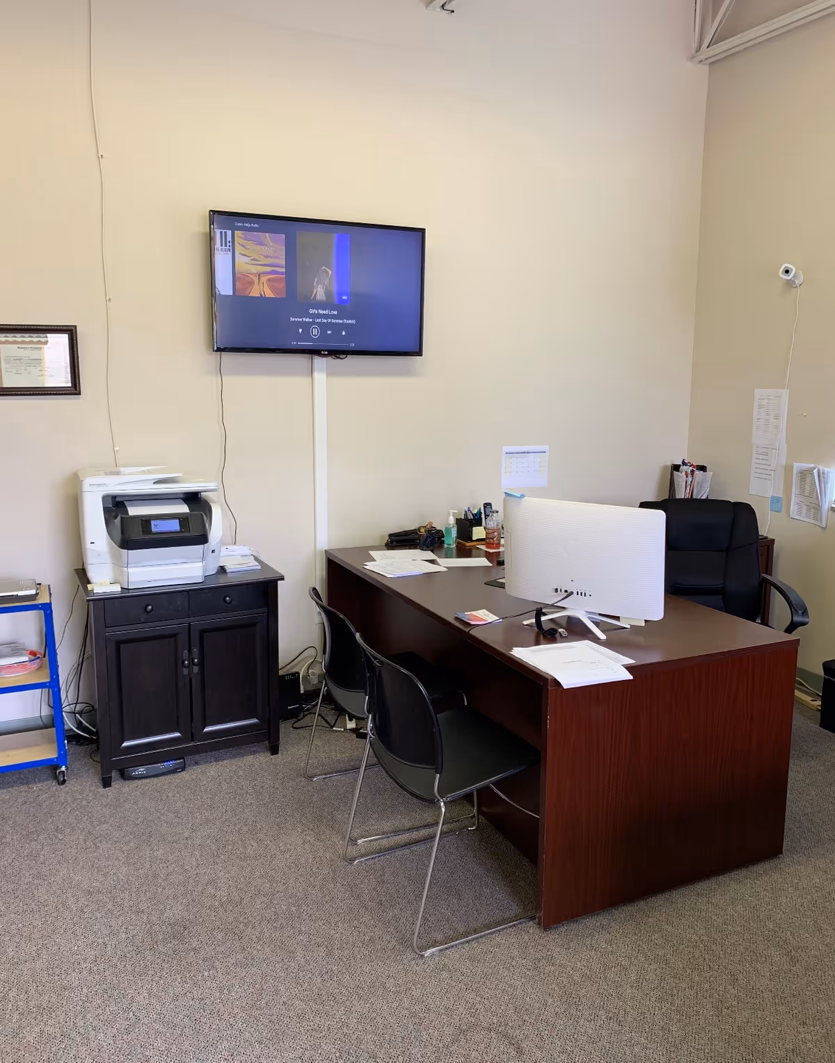 Office desk with computer, printer, and wall-mounted TV in a facility's administrative office.