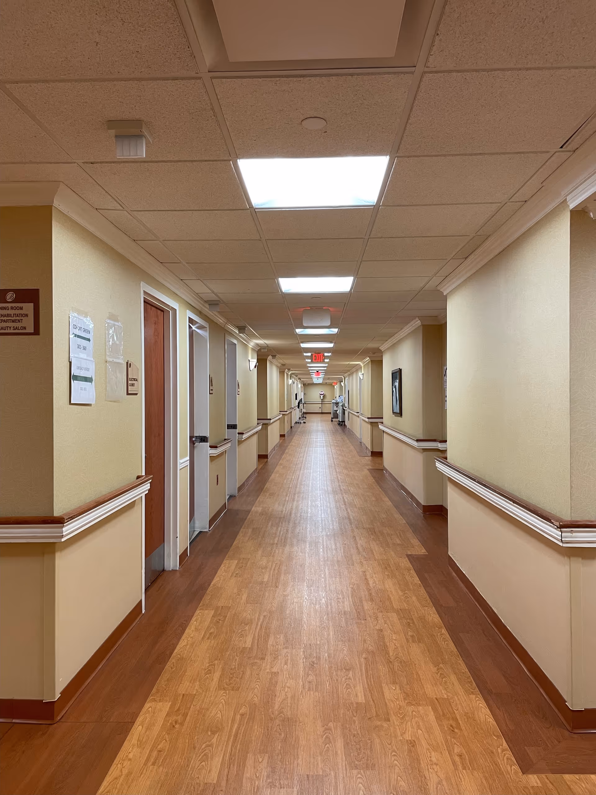 Long brightly lit corridor in a senior care facility with doors on both sides