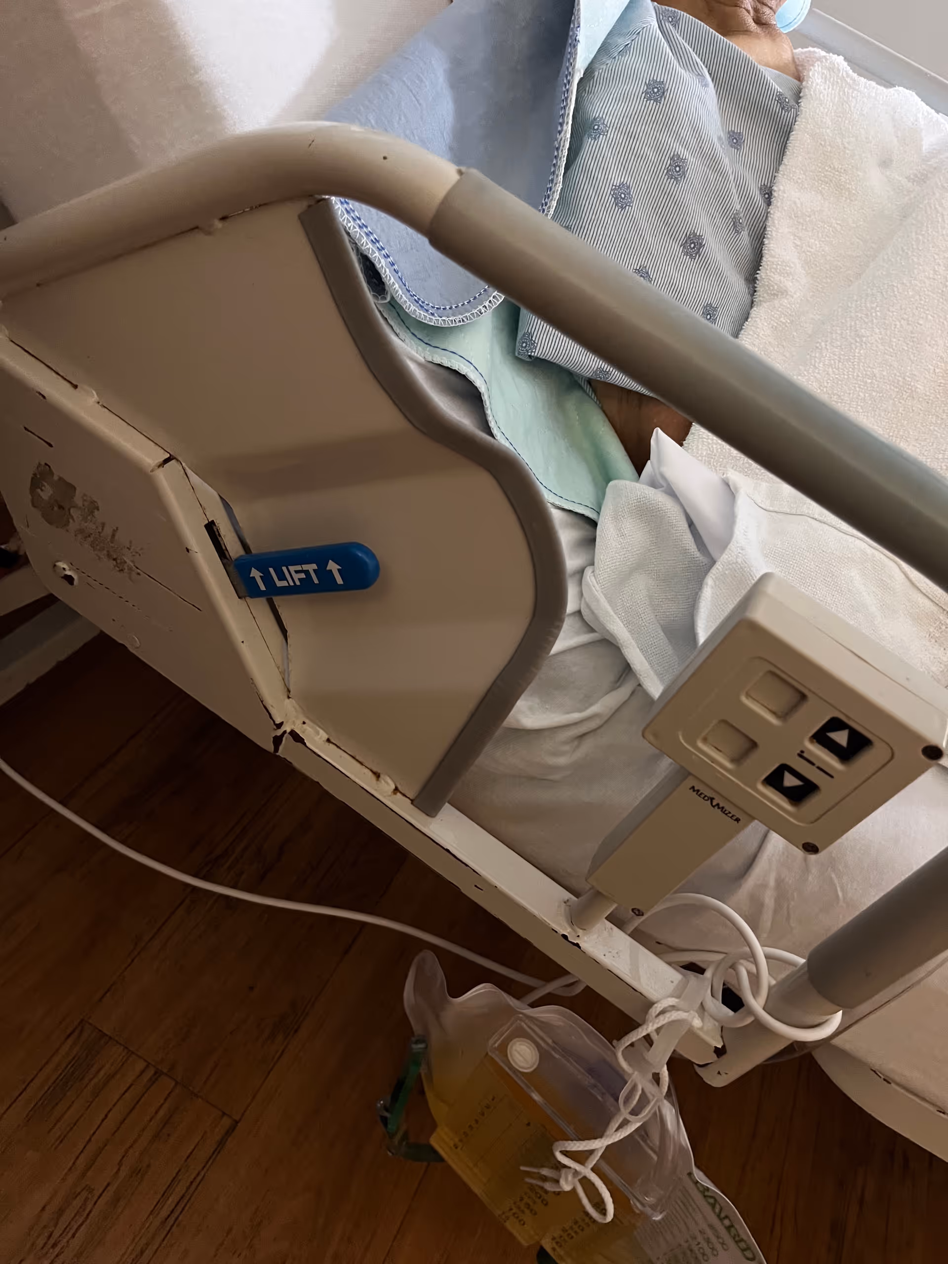 A hospital-style bed with side rails and a control panel in a patient room.