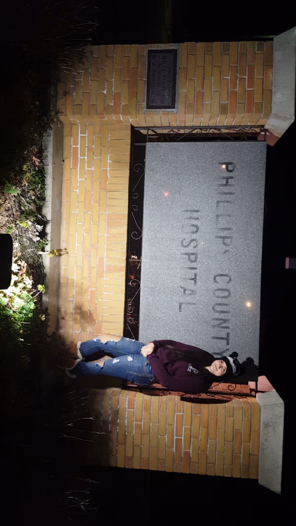 Night exterior of Phillips County Hospital sign on brick wall with a person nearby.