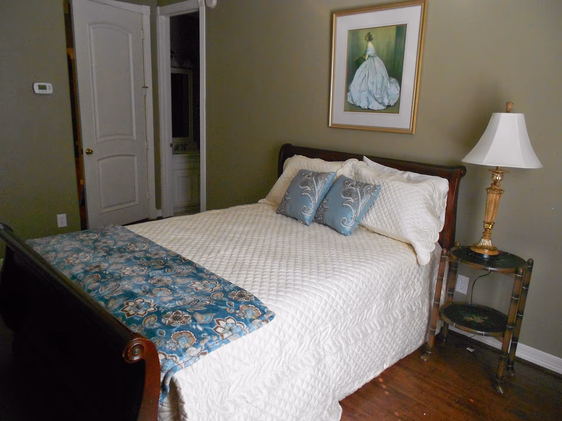 A neatly made bedroom with a bed, pillows, nightstand lamp, and framed artwork.