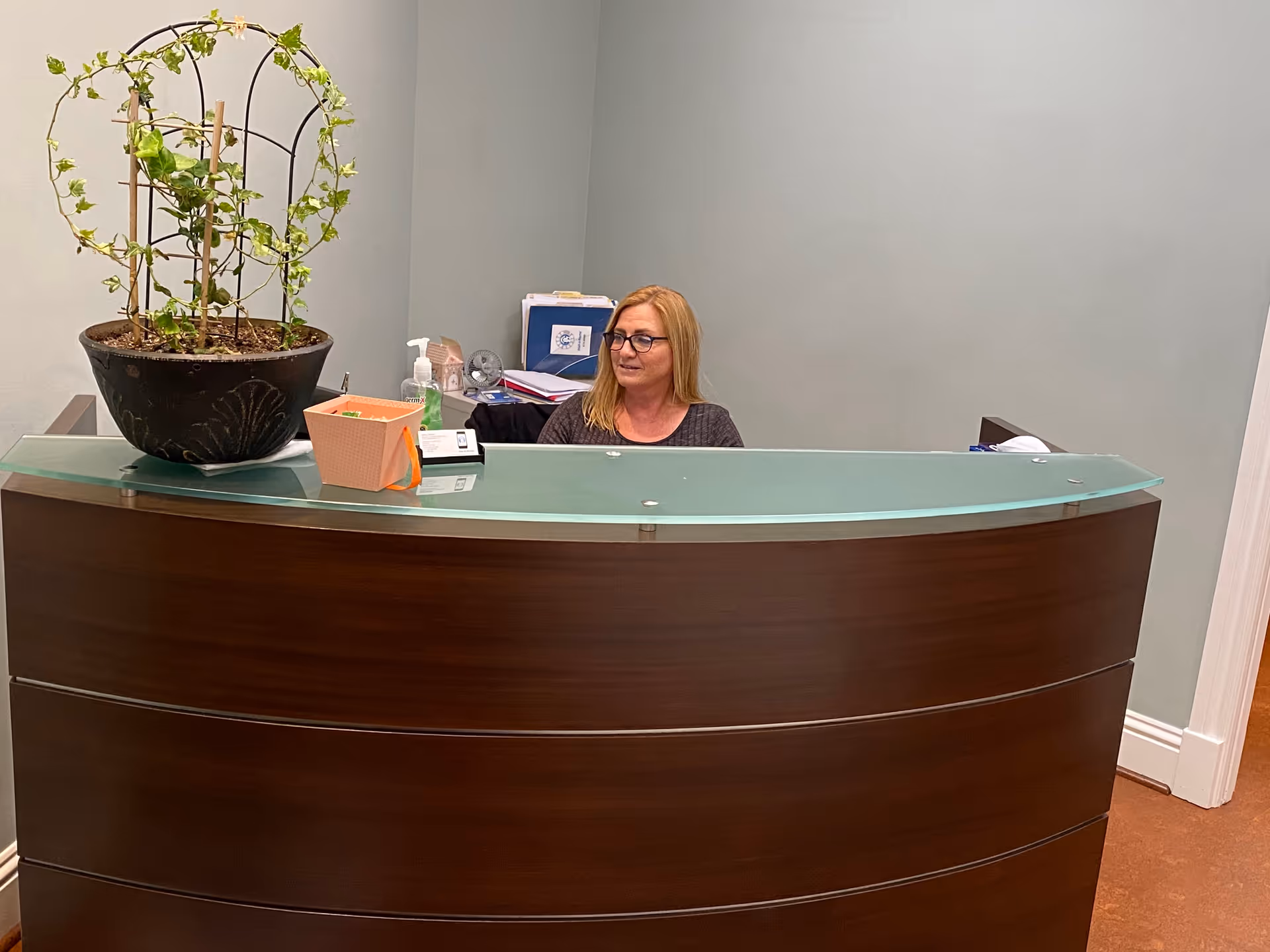 Reception desk with glass top and a smiling woman receptionist inside a pastel-walled facility.