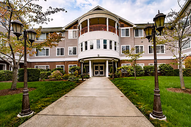 Front view of a three-story senior living building with curved central entrance and lampposts.