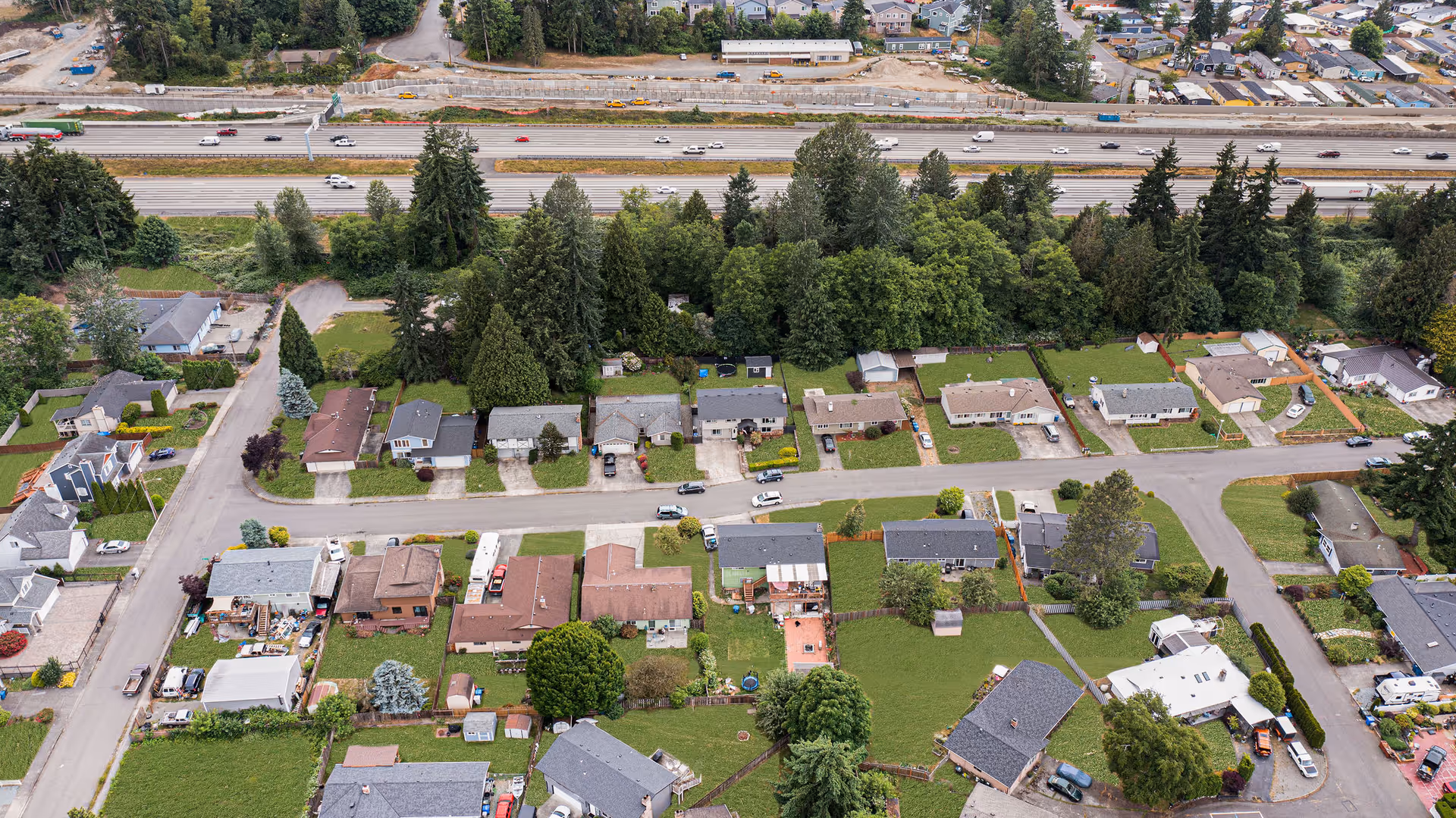 Aerial view of a residential neighborhood with houses, trees, and a highway.