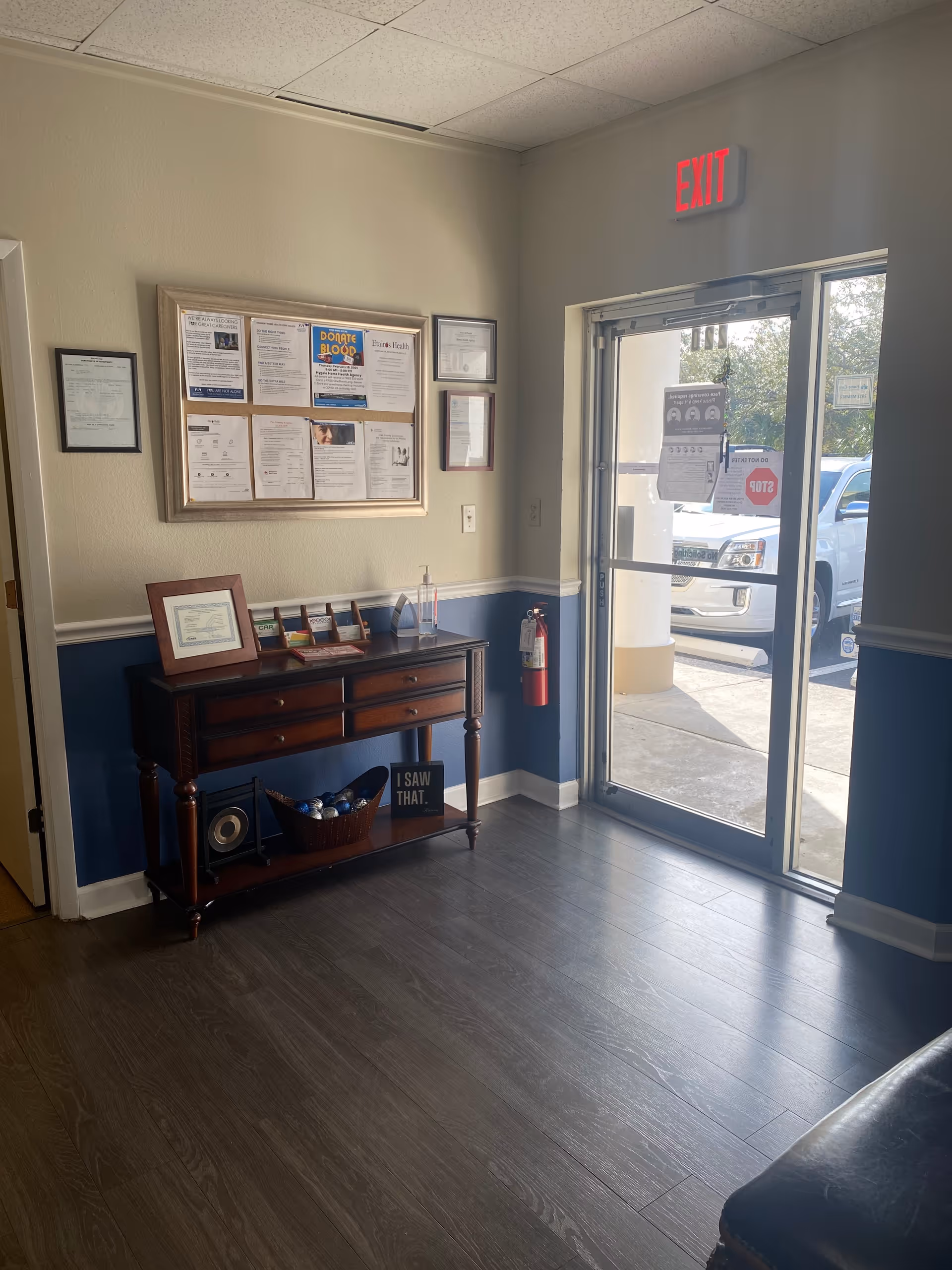 Interior hallway and lobby with bulletin board, console table, and exit door.