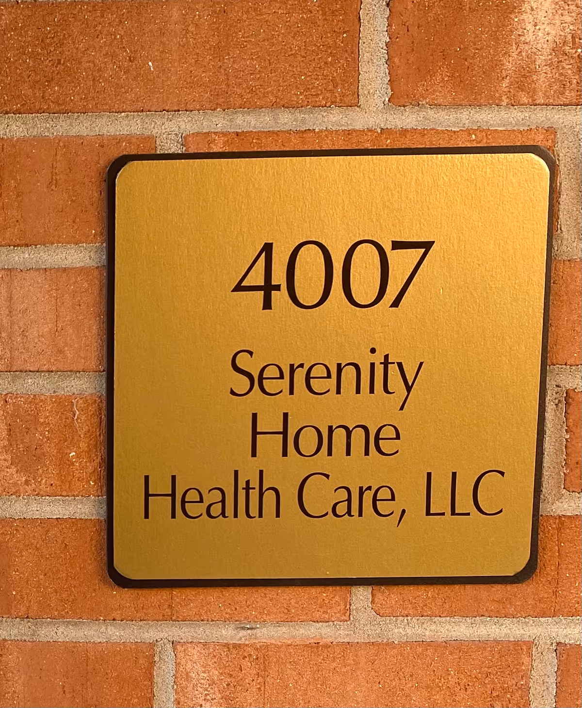 Gold plaque with address 4007 Serenity Home Health Care, LLC on brick wall.