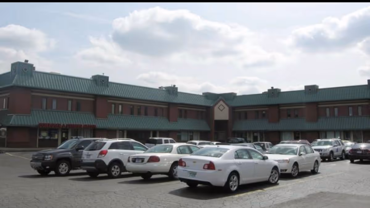 Exterior view of a brick senior living facility with a green roof and parked cars.