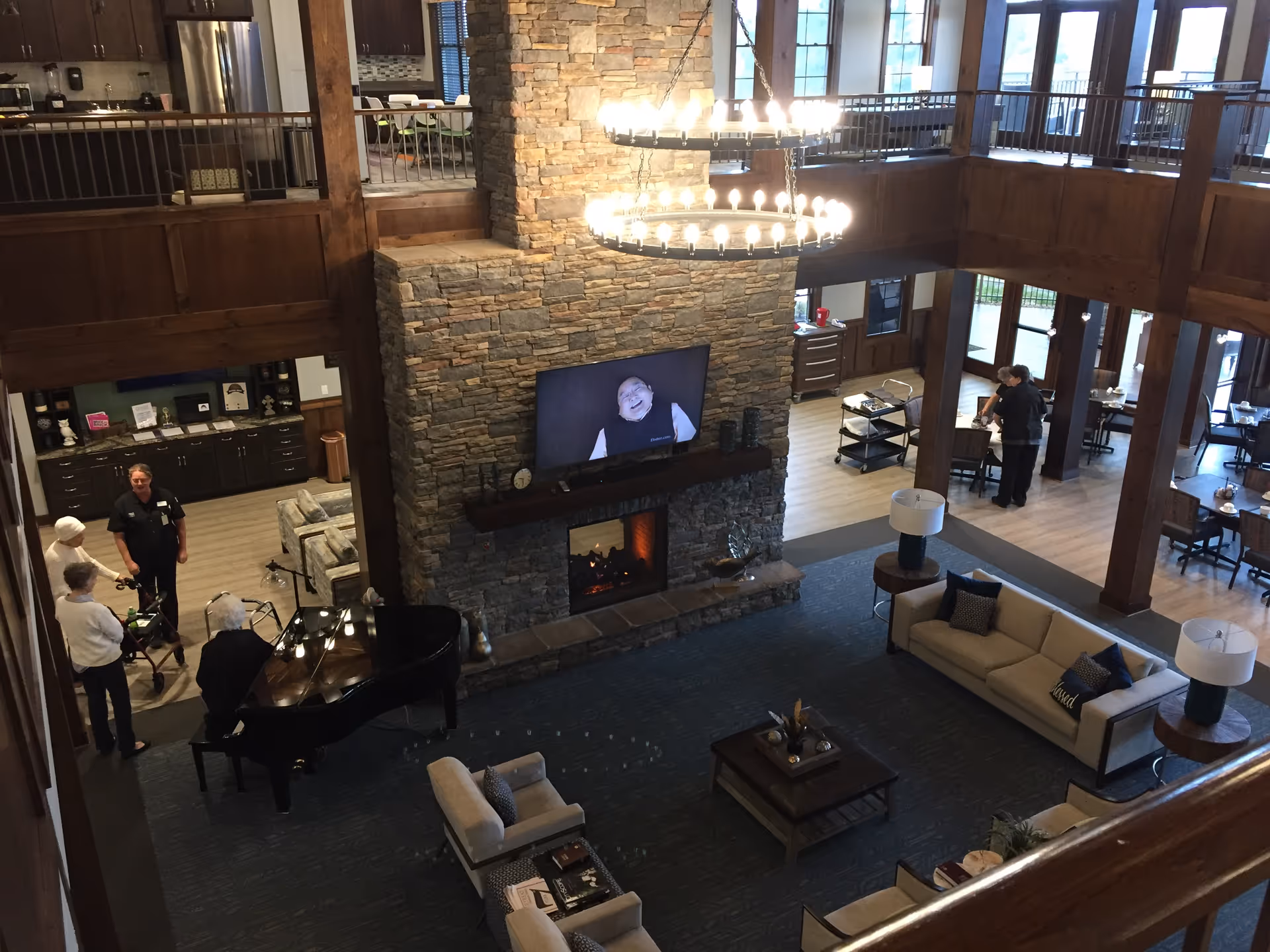 Spacious senior living lobby with stone fireplace, chandelier, and seating around a grand piano