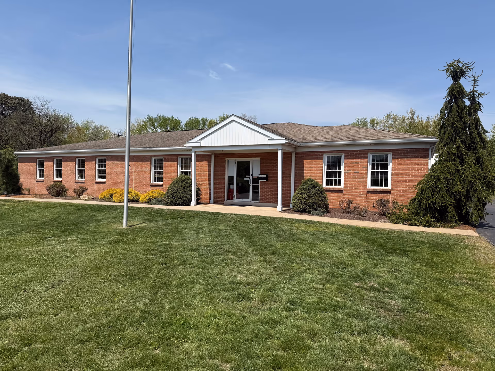 Brick, single-story facility exterior with a front entrance, lawn, and flagpole.