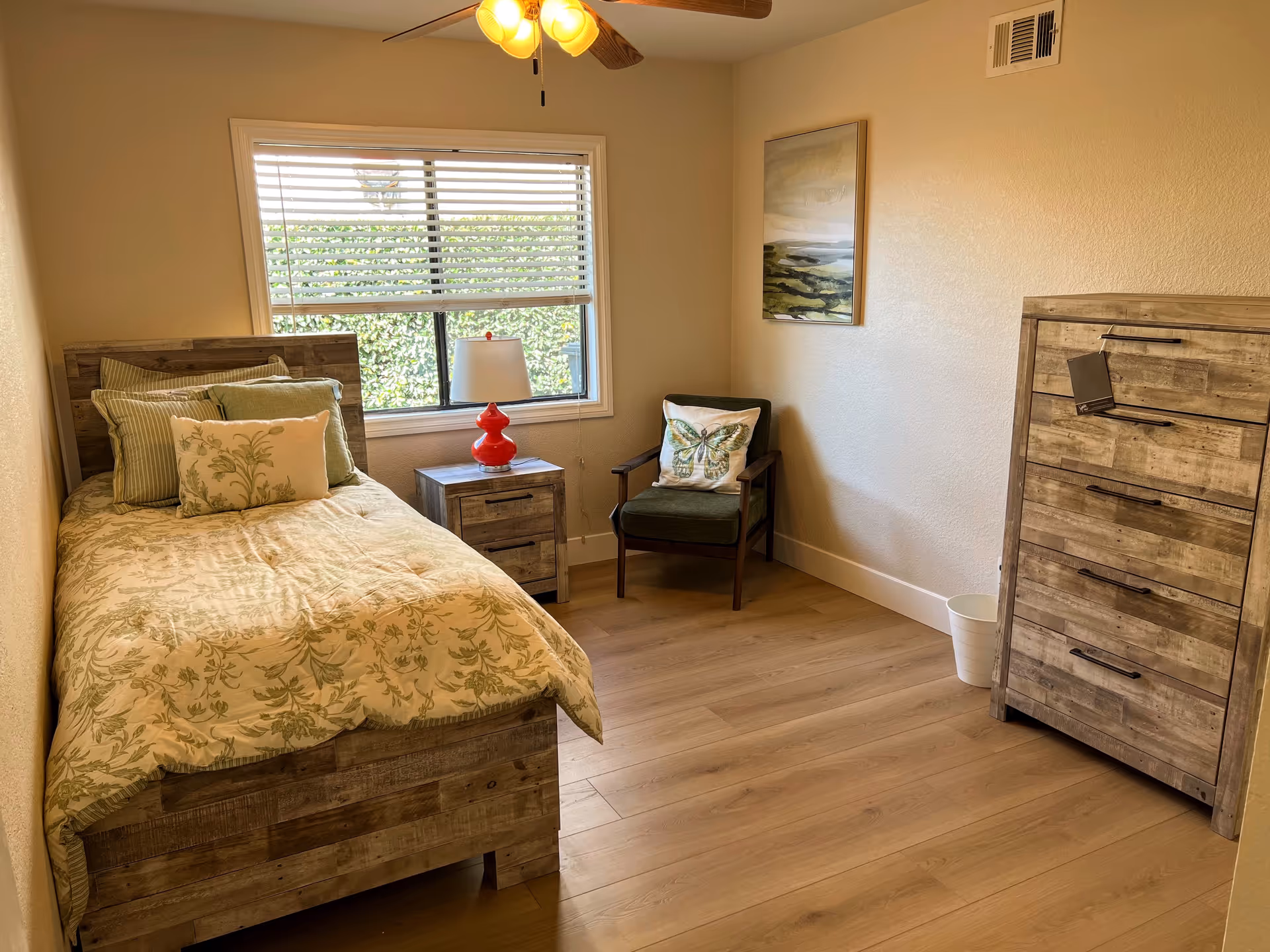 Cozy bedroom with a wooden bed, dresser, chair, and window blinds.