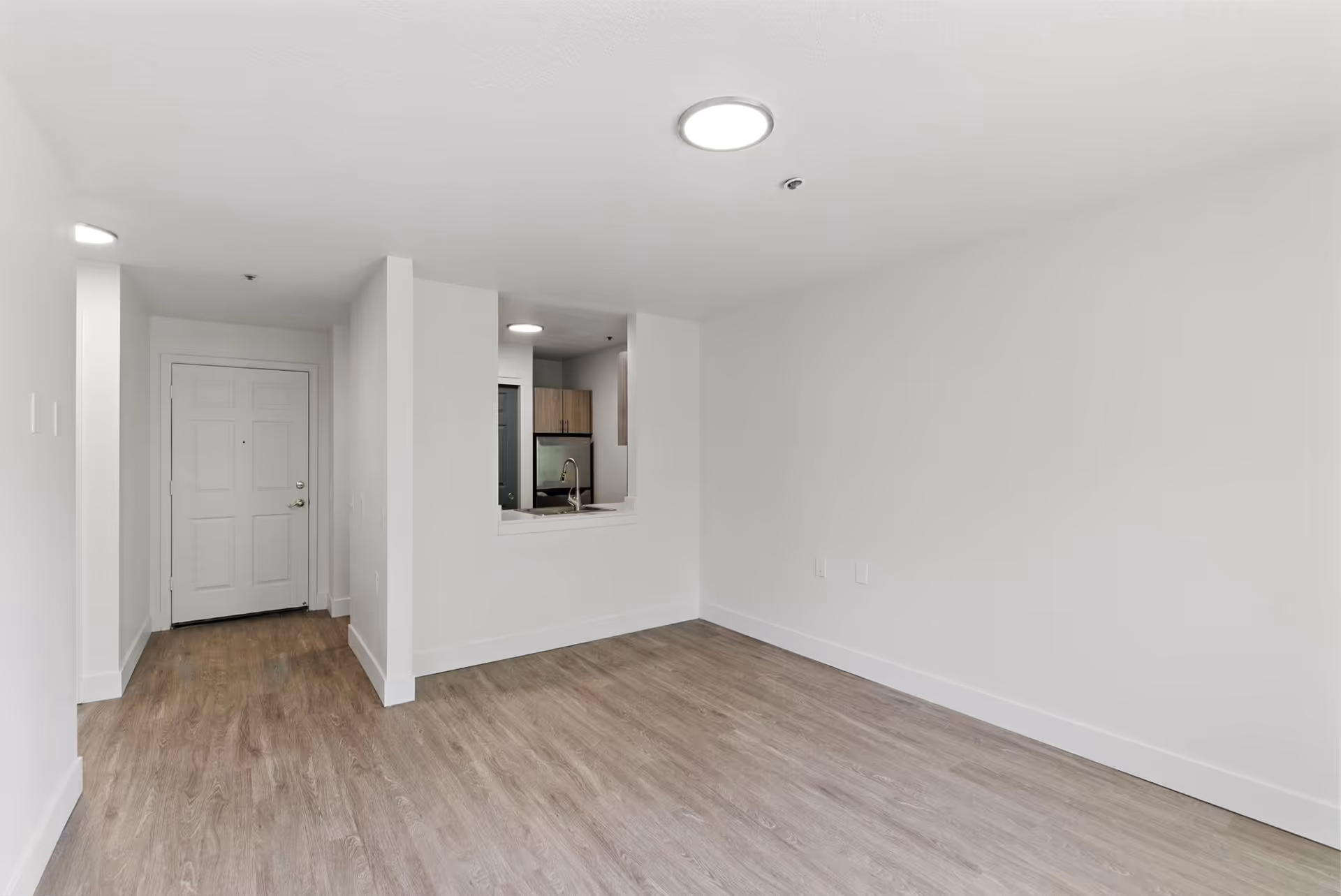 Bright empty living area at Solista Milwaukie with wood floors and a kitchen pass-through.