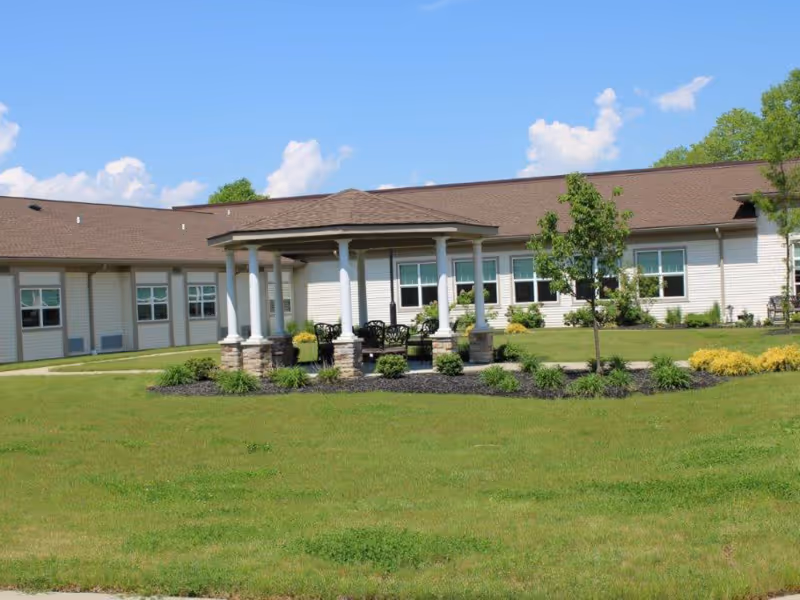 Single-story care facility building with a central gazebo and landscaped lawn under a blue sky.