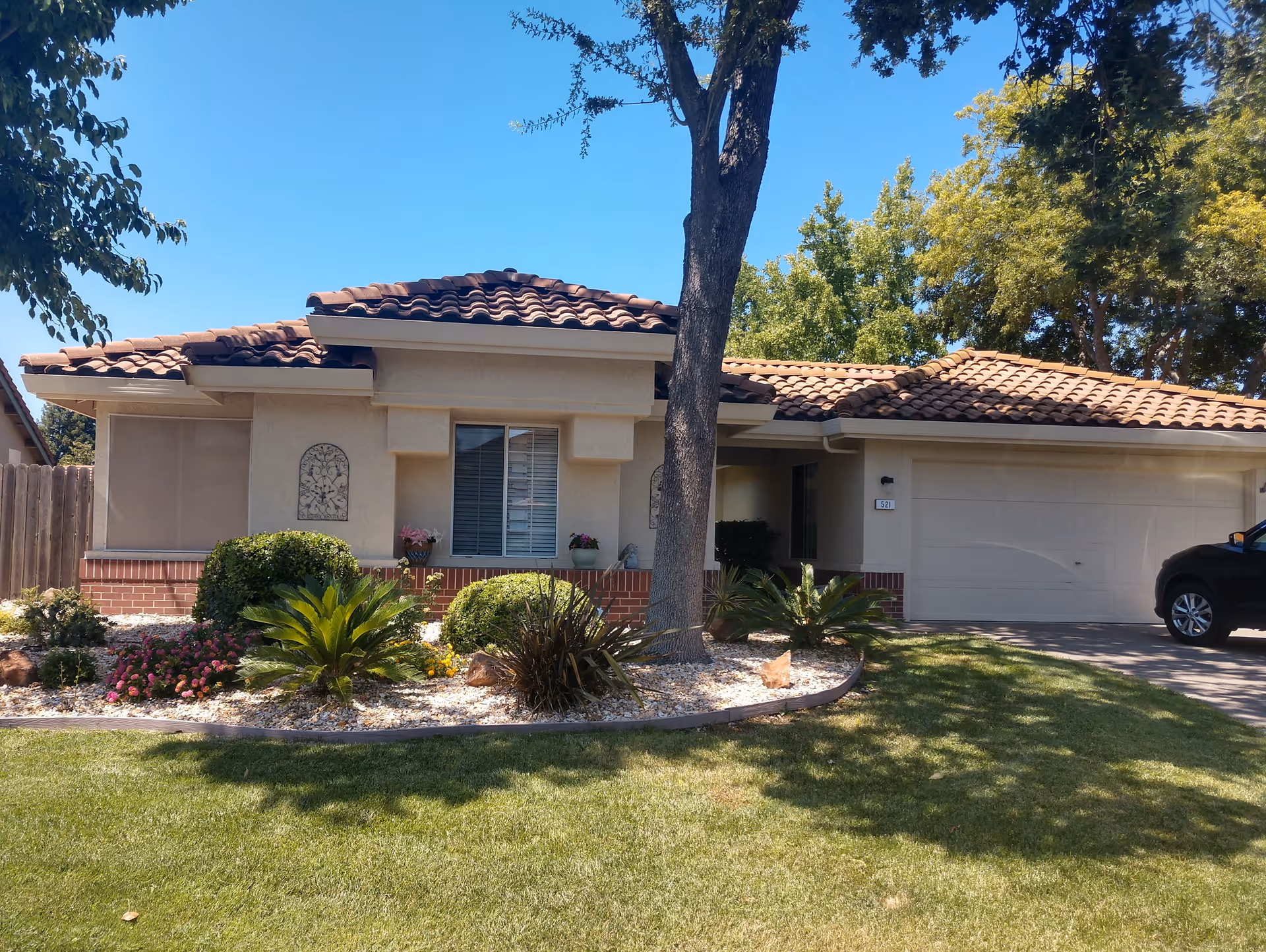 Front exterior of a single-story stucco house with a tiled roof, attached garage, tree, and landscaped front yard.