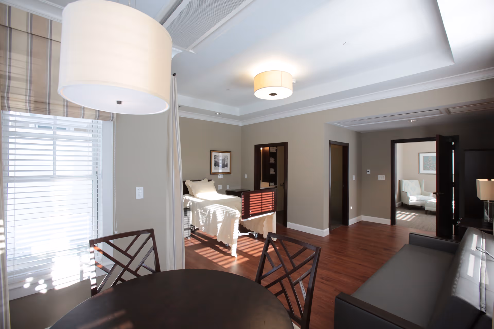 Interior common area of a senior living facility with sofa, dining table, and bed visible.