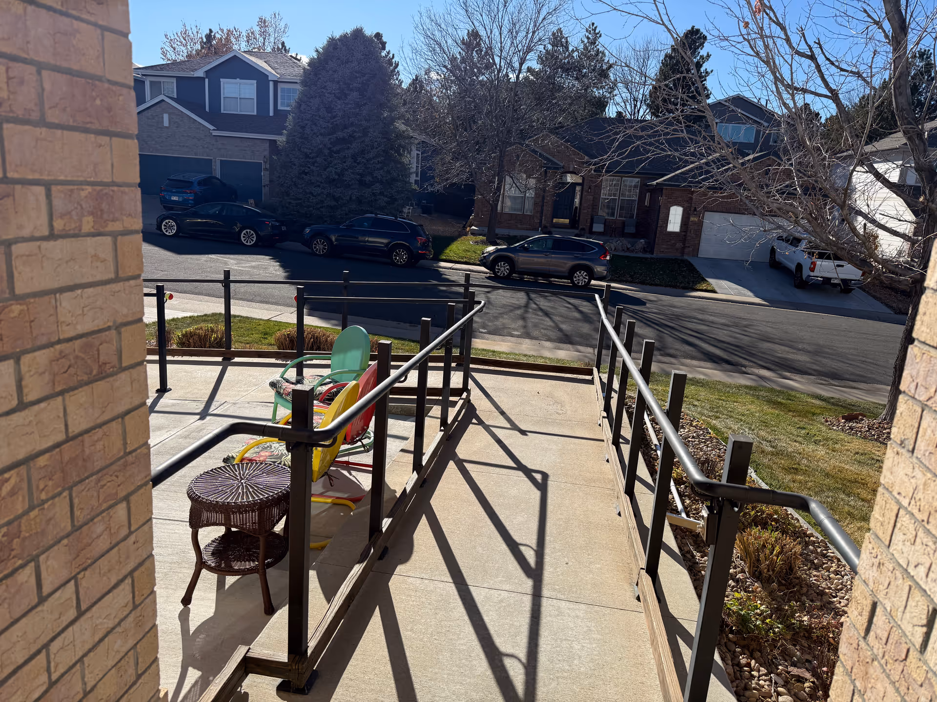An outdoor ramp to the entrance with colorful chairs and a wicker table.