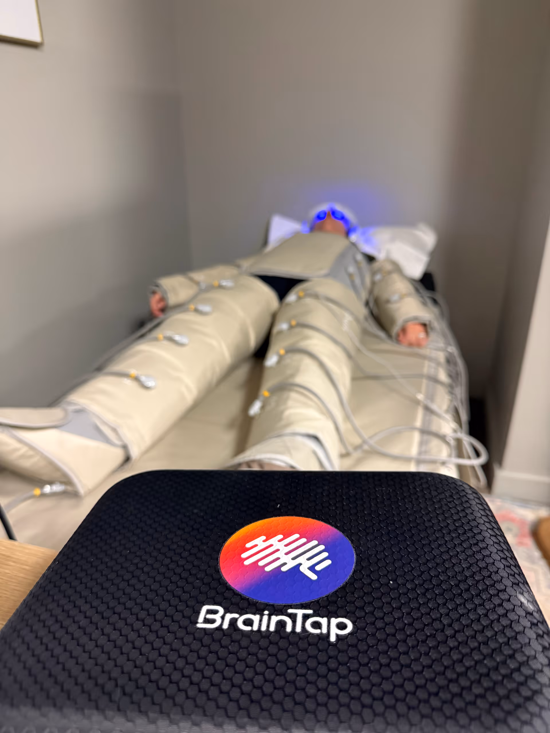 Person lying on a padded therapy bed with BrainTap device in foreground.