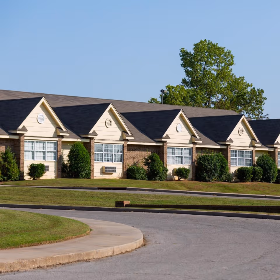 Row of beige, single-story buildings with peaked roofs and landscaped front lawn.