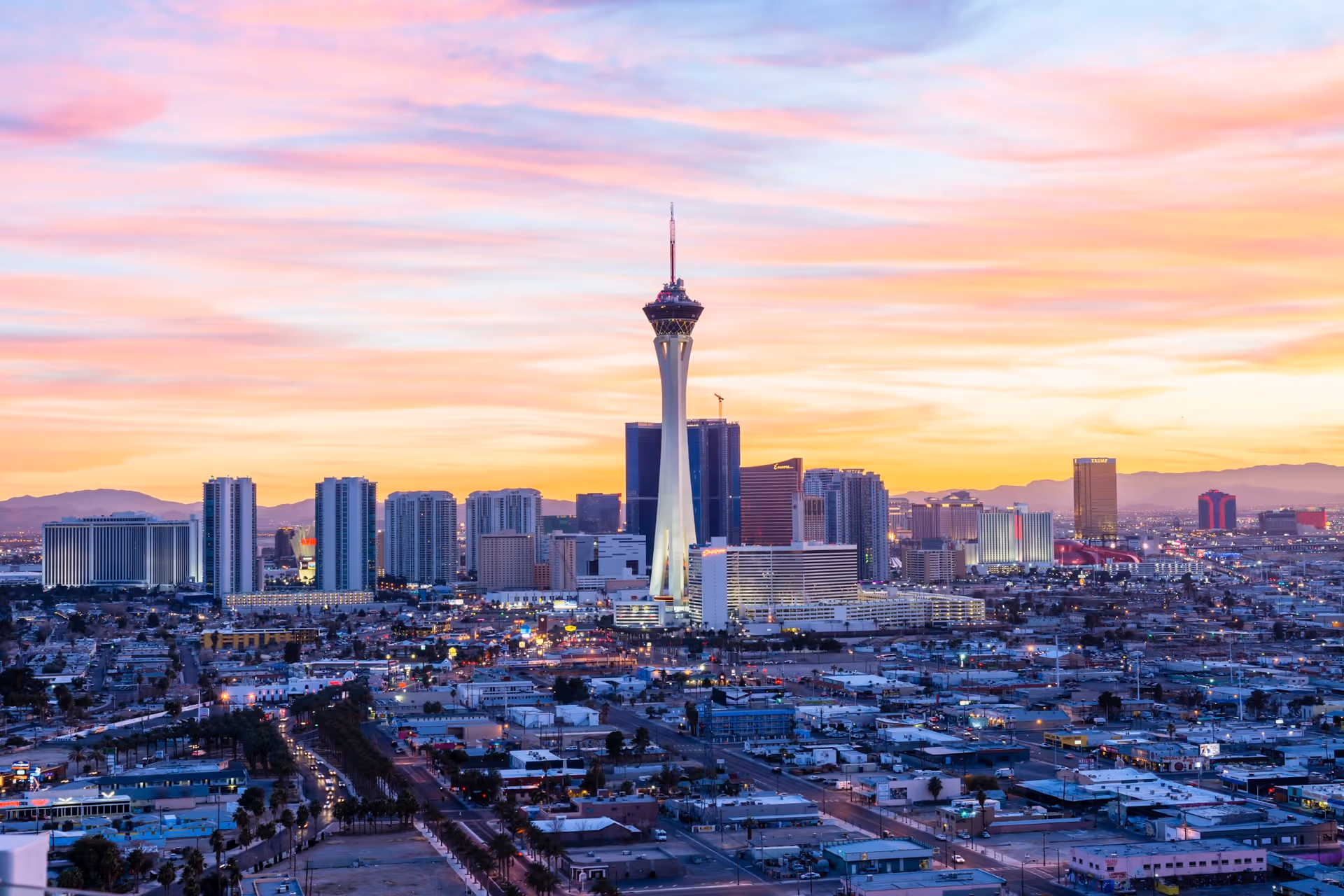 A city skyline at sunset featuring a tall central tower and surrounding buildings.