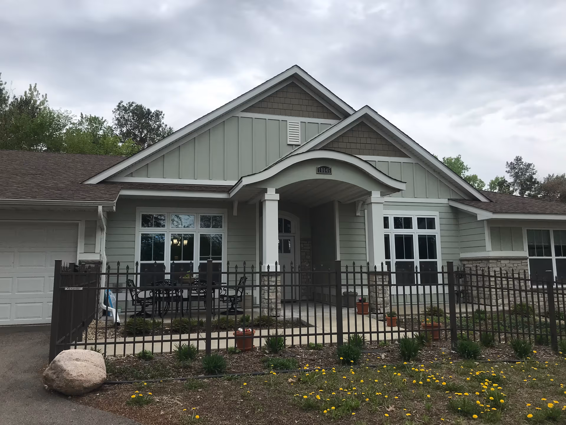 Exterior view of a pastel green senior living facility with gate and porch seating.
