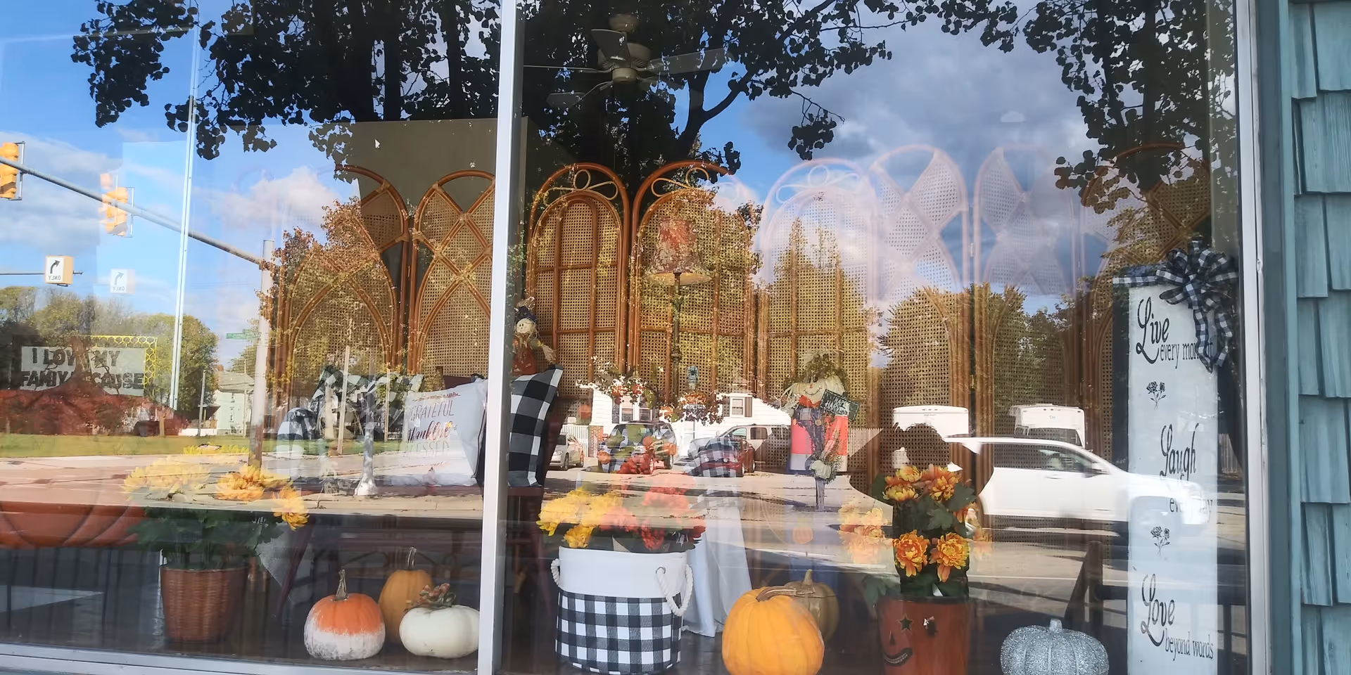 Storefront window display featuring pumpkins and autumn decorations, reflecting a street scene.
