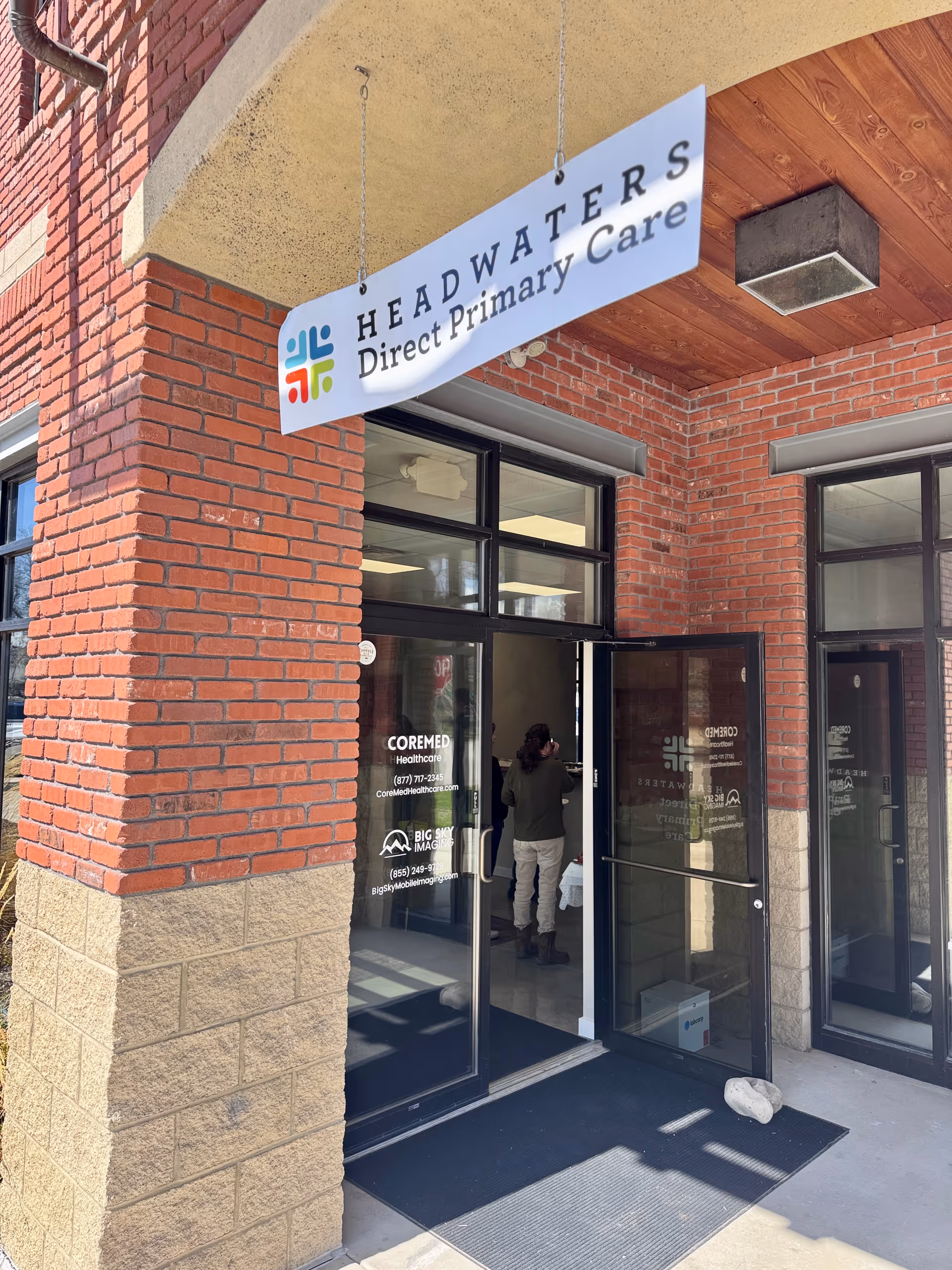 Brick building exterior with glass doors and a hanging Headwaters Direct Primary Care sign.