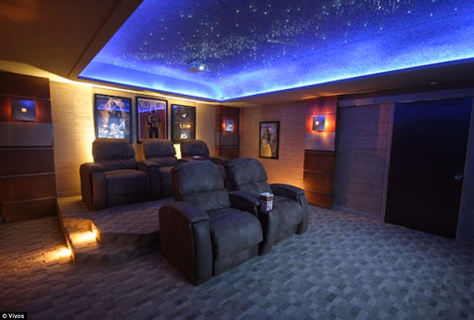 Dimmed theater-style lounge with reclining chairs, blue ceiling lighting, and movie posters.