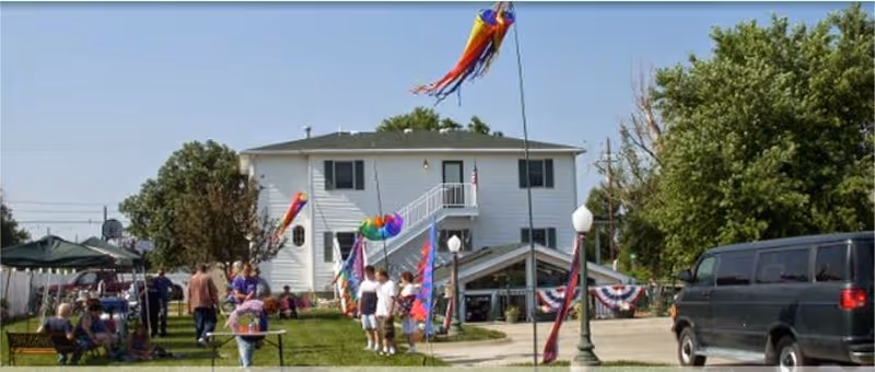 Exterior view of a two-story facility with colorful banners and residents outside.