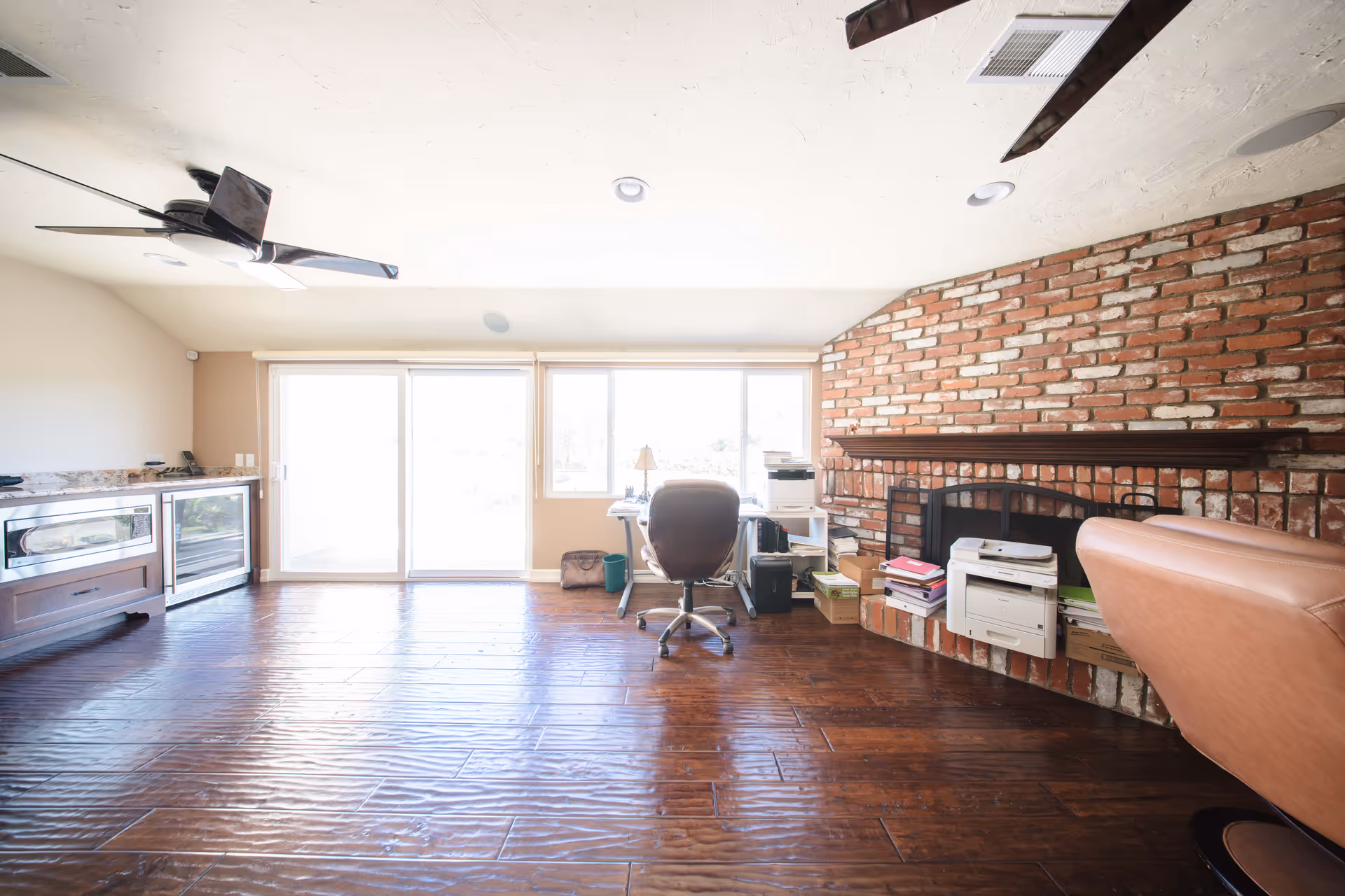 Spacious living area with brick fireplace, desk, office chair, and large sliding glass doors.