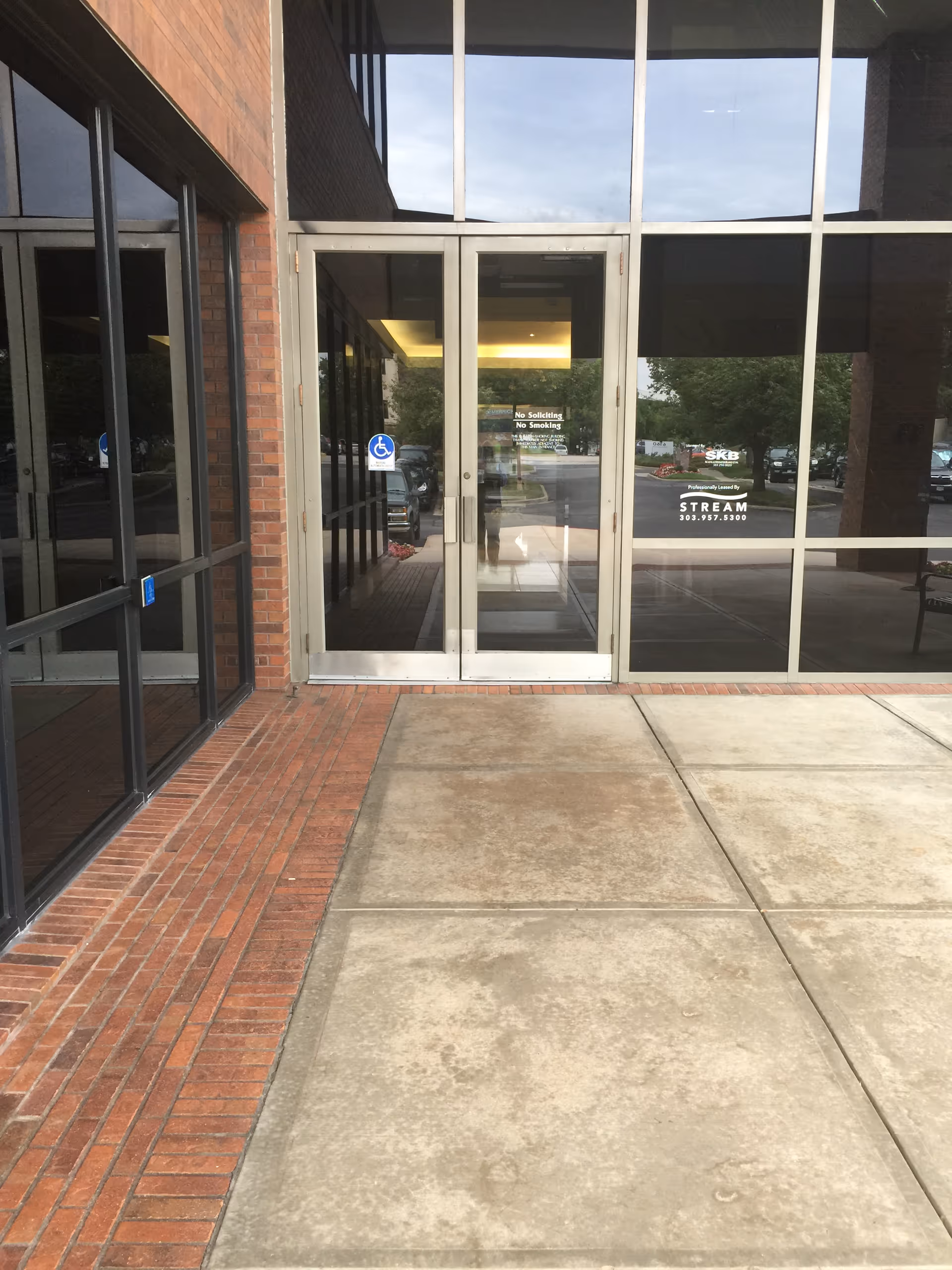 Glass entrance doors with brick exterior and a concrete walkway leading to the building.
