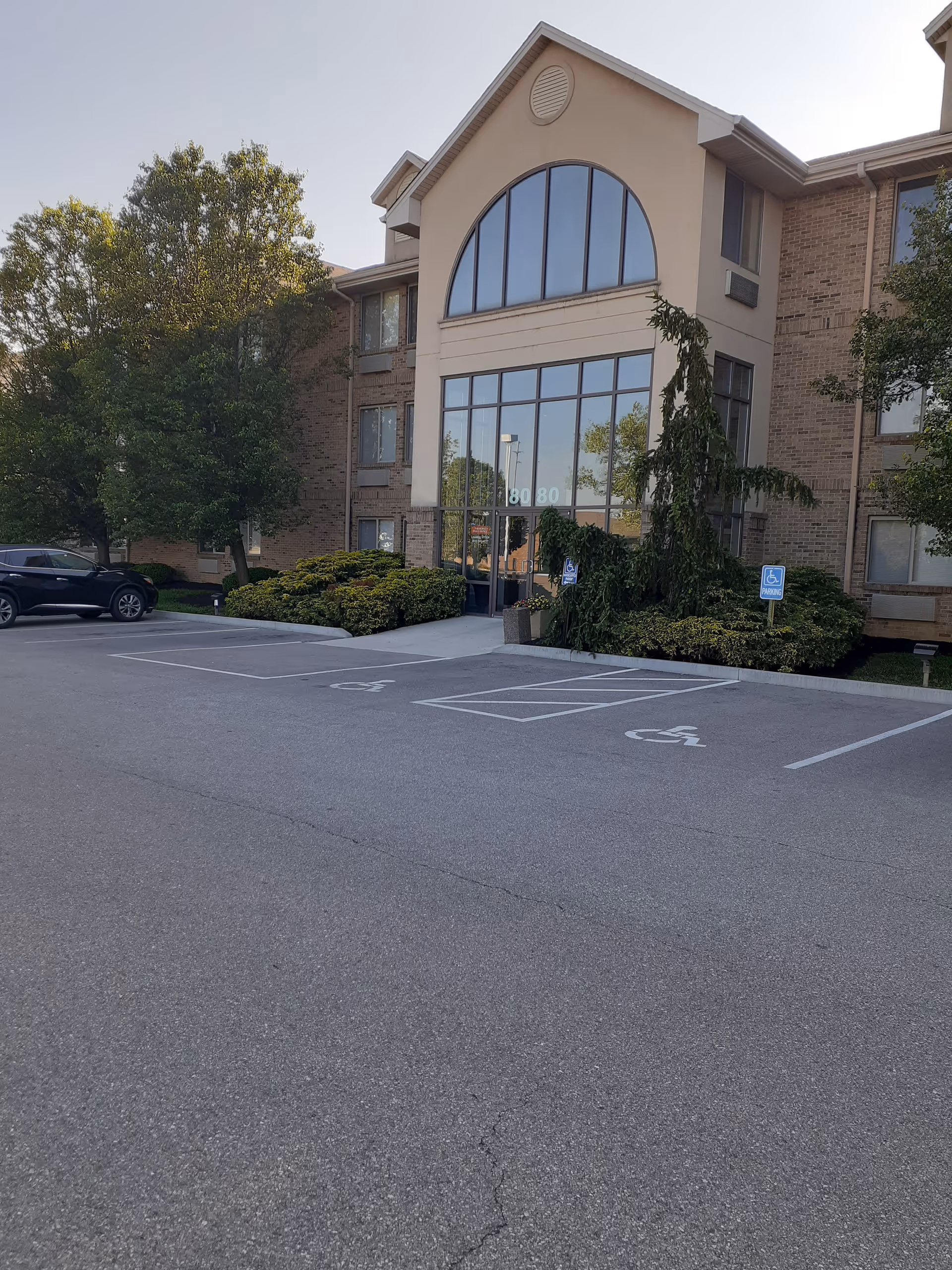 Front exterior of a senior living facility with a large arched glass entrance and parking.