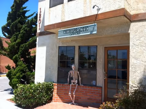 Exterior view of a chiropractic office storefront with a skeleton model beside the window