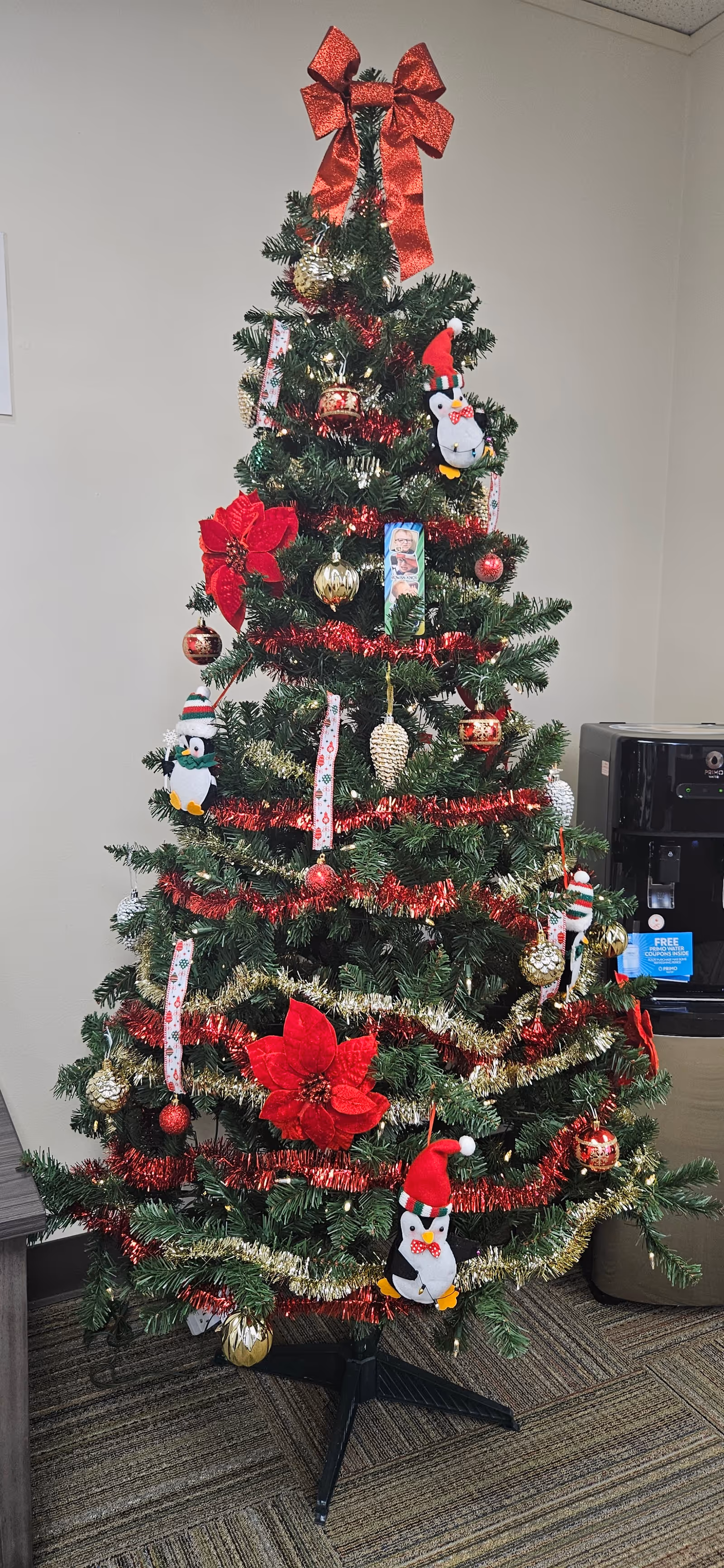 Indoor Christmas tree with red ribbons and gold ornaments in a common room.