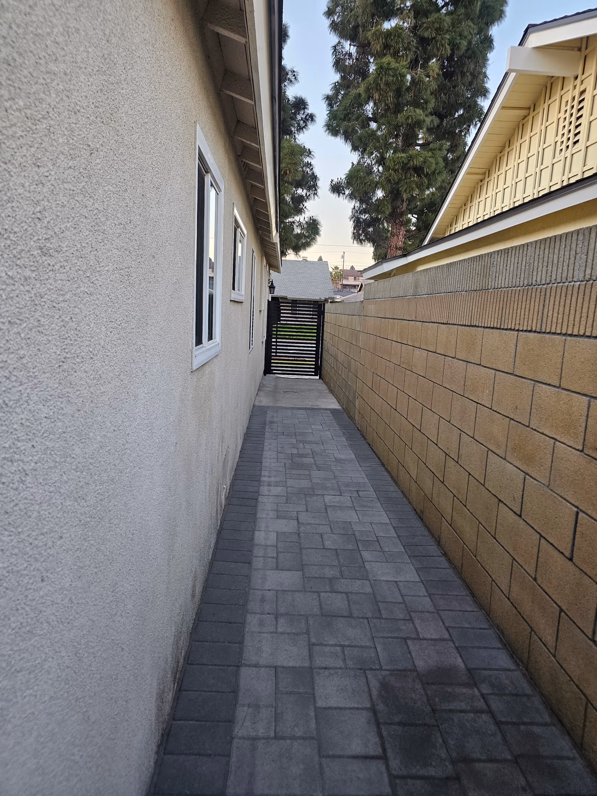 Narrow outdoor walkway between beige stucco wall and brick wall with a gate ahead.