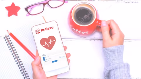 A hand holds a phone displaying Doctor Alexa app with notebook and coffee mug.