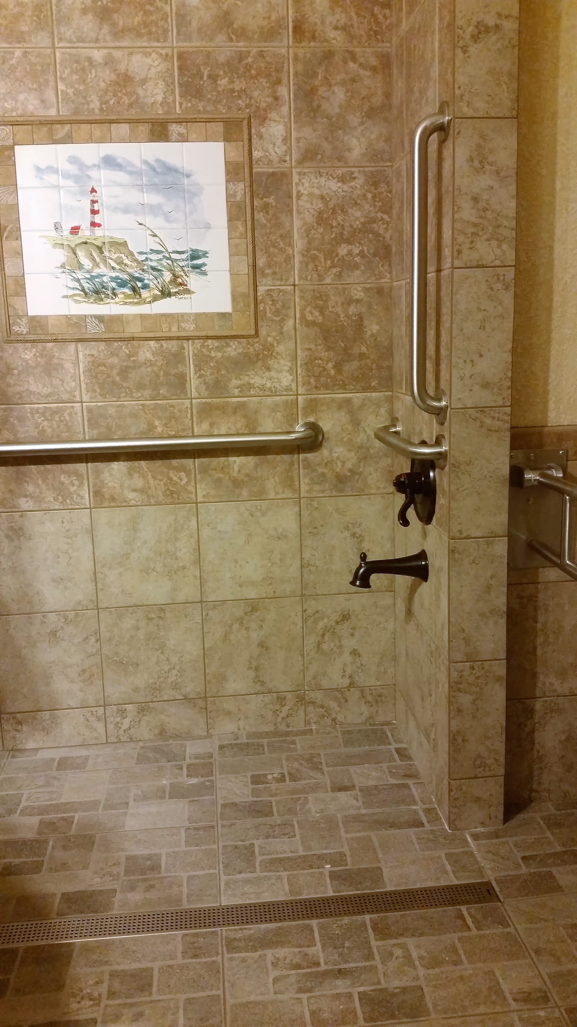 Tiled bathroom interior featuring grab bars, a handheld shower, and wall-mounted artwork.