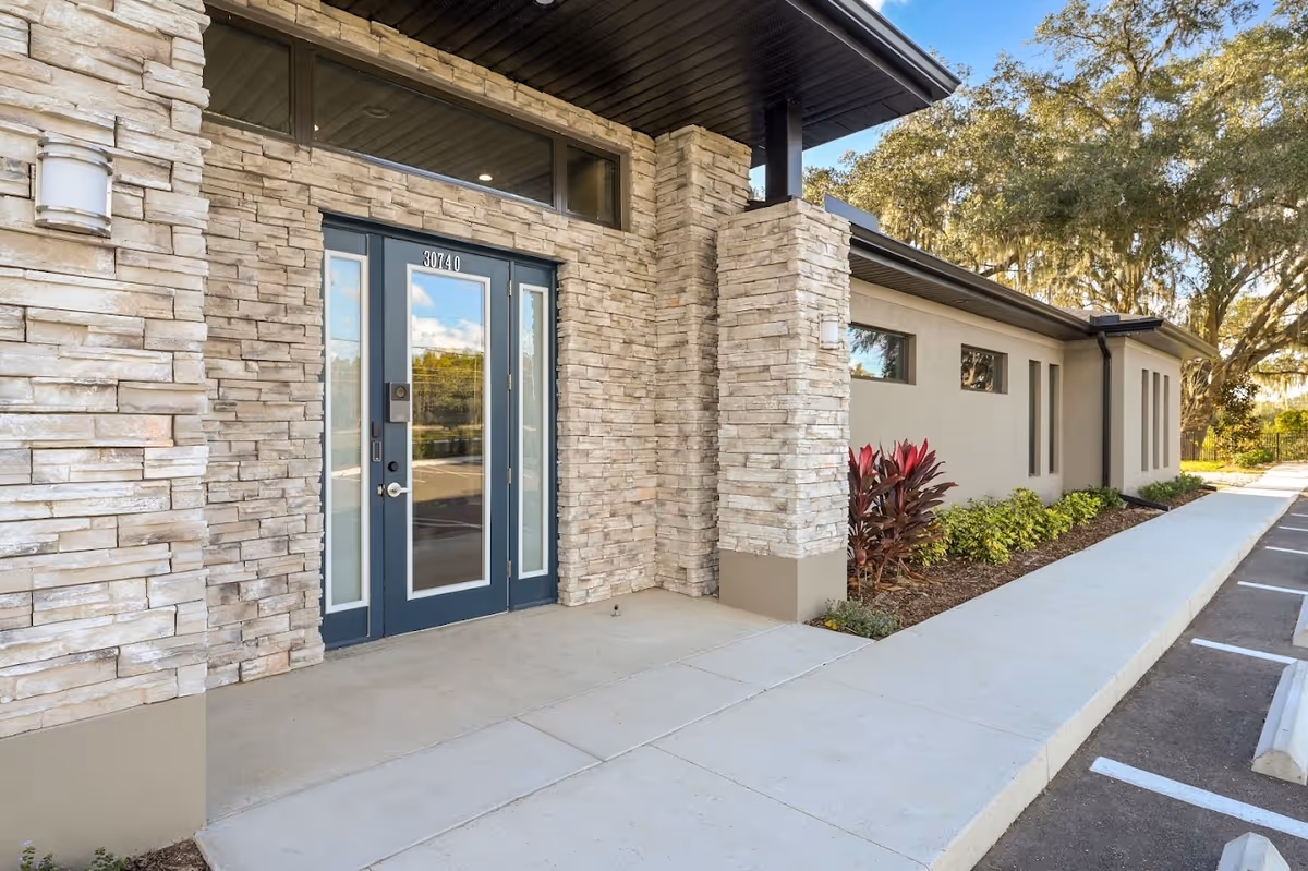 Stone-clad building front with glass double doors and a concrete entry walkway.