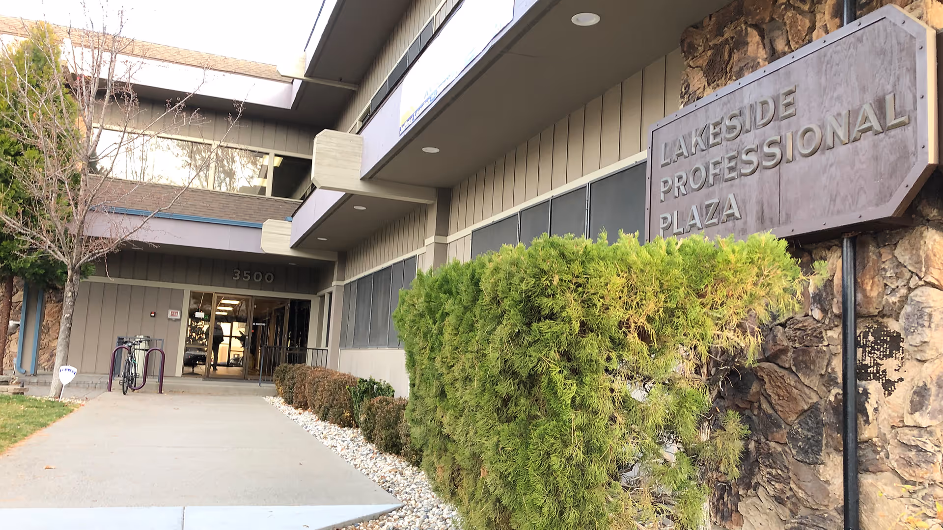 Exterior view of a building entrance with signage and trimmed hedges.