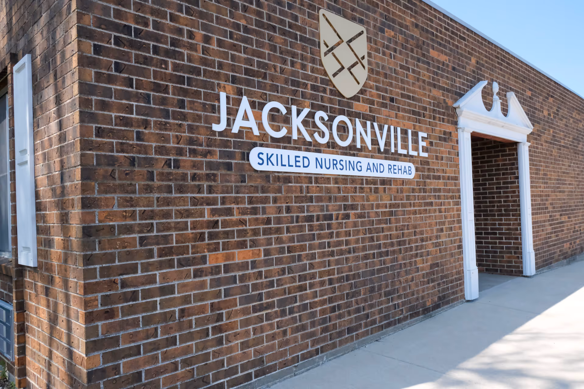 Exterior view of a brick building with a sign that reads 'Jacksonville Skilled Nursing and Rehab' and a decorative white entrance frame.