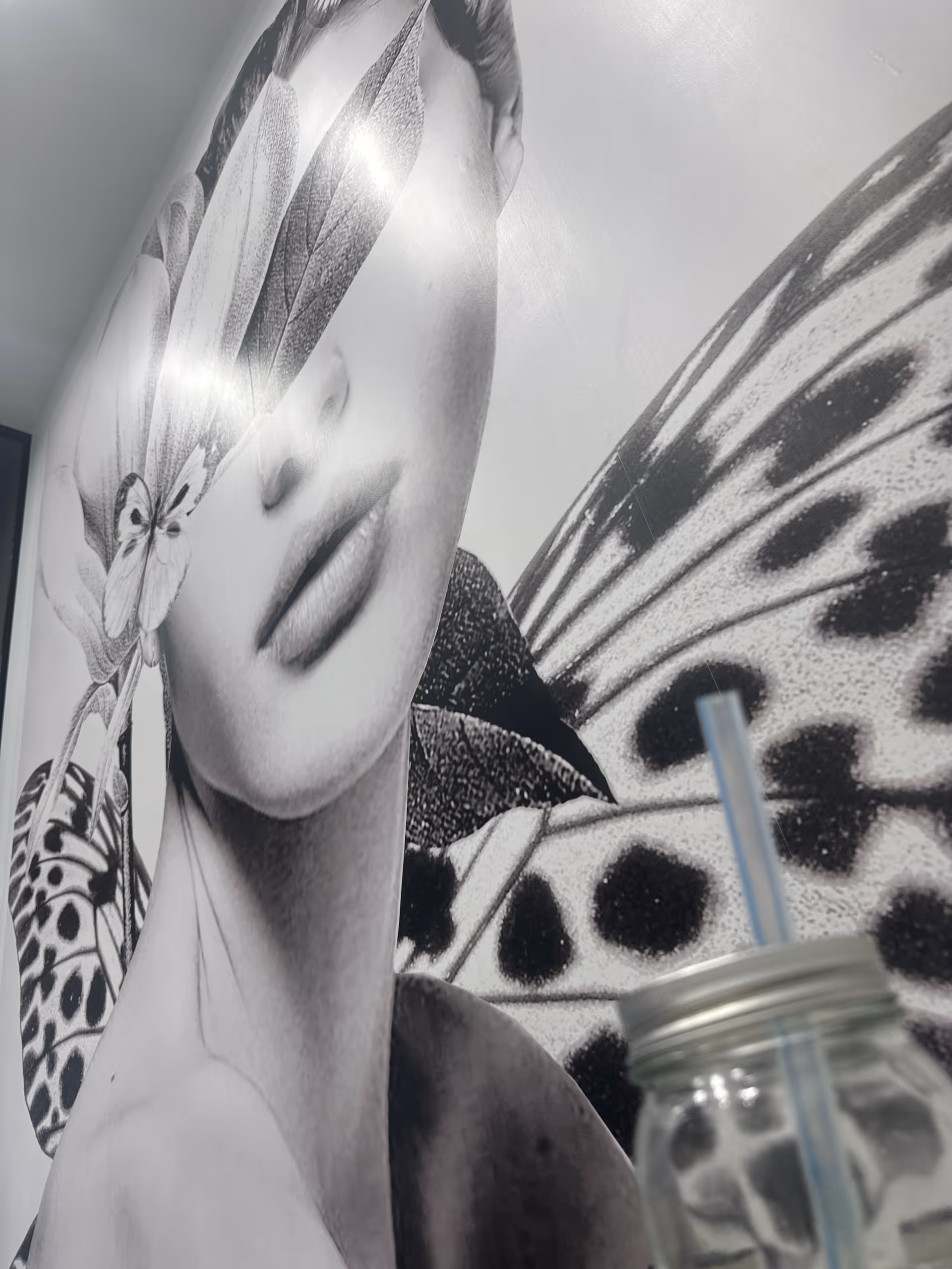 Black-and-white mural of a woman's face with butterfly wings on the wall; a jar foreground.