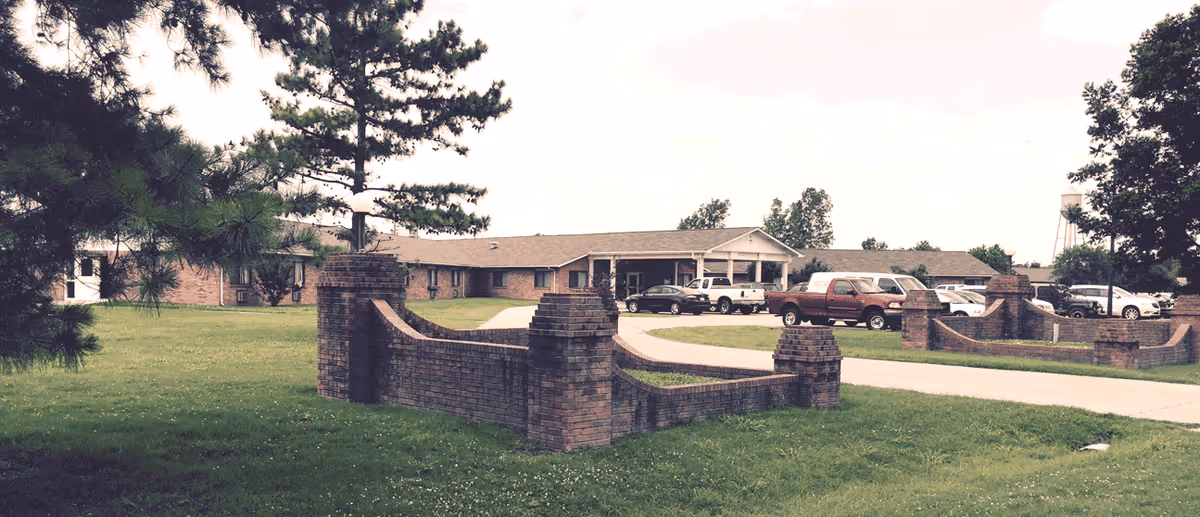Exterior view of Gideon Care Center with brick entrance walls, driveway, and parked cars.